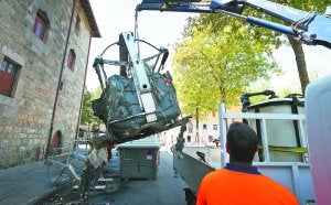 Un operario retira uno de los contenedores calcinados en la plaza Balda junto al palacio Irizar, cuya fachada quedó ennegrecida por el humo. :: LOBO ALTUNA/