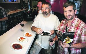 Ritxar y Josema, con el pintxo en una mano y el nuevo libro en la otra, en la barra del bar Oilarra. :: LIMIA/