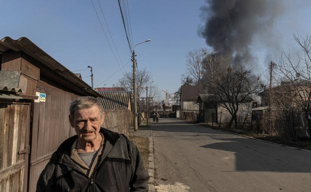 An old man walks through one of the outskirts of kyiv while a bombardment takes place.