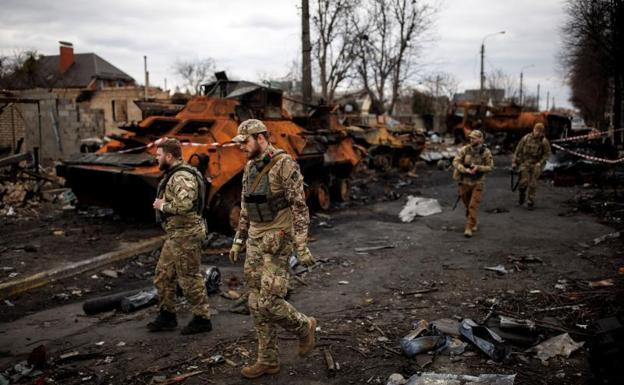 Several soldiers walk through what remains of the streets of Bucha. 