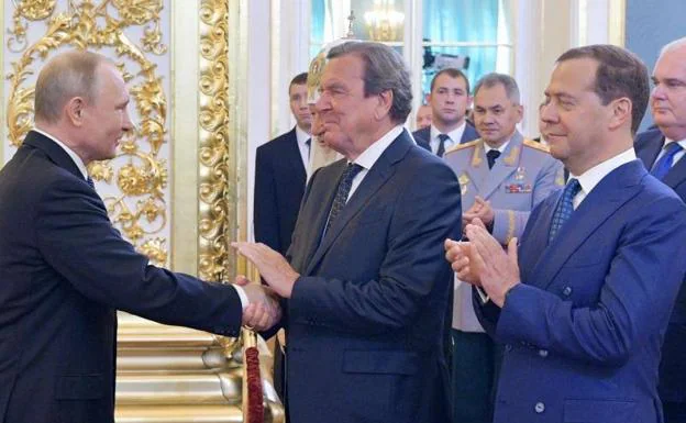 Vladimir Putin shakes hands with former German Chancellor and Social Democratic leader Gerhard Schröeder in the presence of Russian Prime Minister Dmitry Medvedev in 2018
