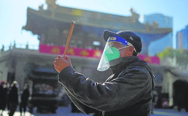A man wearing a protective mask and face shield worships at the Jingan Buddhist temple.